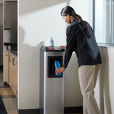 A woman uses the Cintas WaterBreak water cooler machine in the break room of her job.
